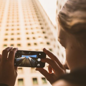 Person photographing skyscraper with smartphone.