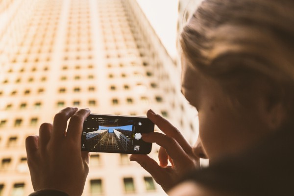 Person photographing skyscraper with smartphone.