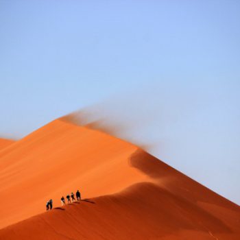 People walking on a large desert dune.