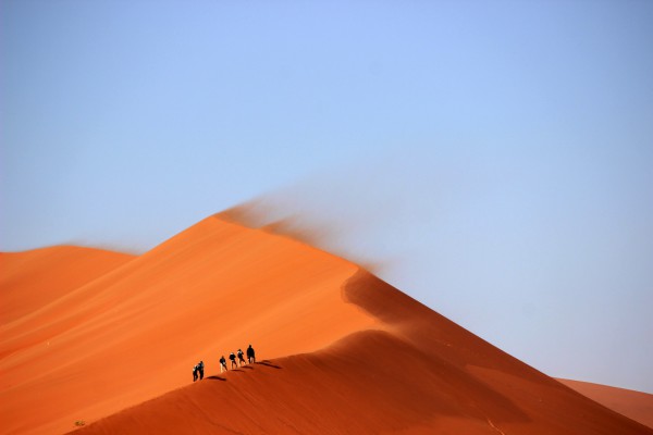 People walking on a large desert dune.